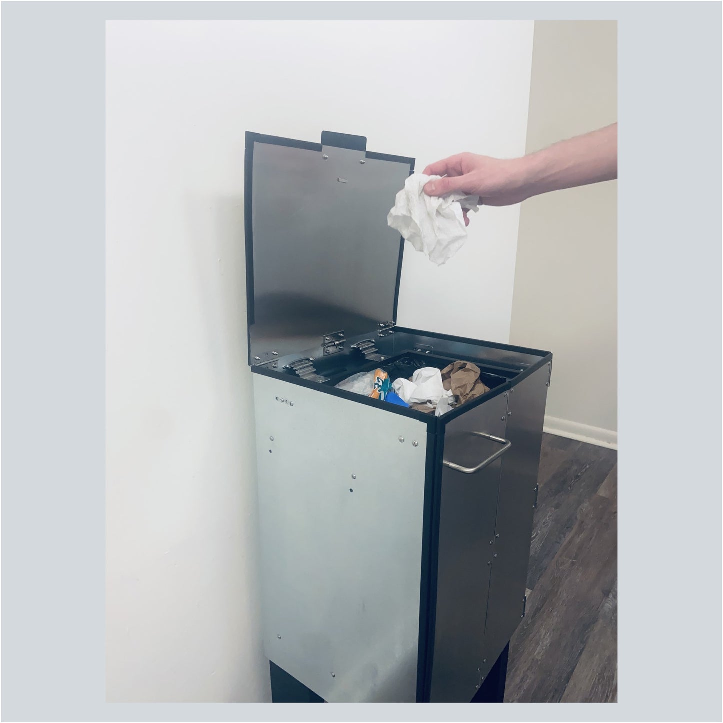 The DorrCan in a kitchen with the lid open adn door closed, trash is being inserted into the trash can